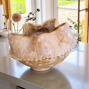 Könnte beinhalten: Eine große, beige dekorative Schale mit einem einzigartigen, wellenförmigen Rand. Die Schale hat eine strukturierte Oberfläche und steht auf einer grauen Arbeitsplatte. Die Schale wird wahrscheinlich zu Dekorationszwecken oder als Mittelstück verwendet.