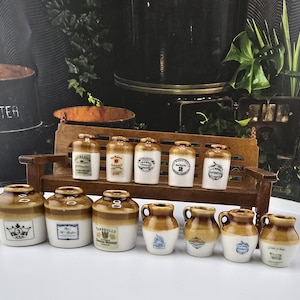 May include: A collection of miniature ceramic jars and jugs, featuring a two-tone brown and white glaze. Some jars have labels with text, and others have decorative elements. The items are arranged on a small wooden bench.