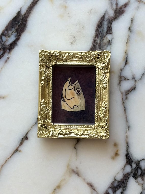 A tiny ornate-framed fish head portrait that treats seafood with the gravitas of a Renaissance painting — absurdist miniature art for your fridge.