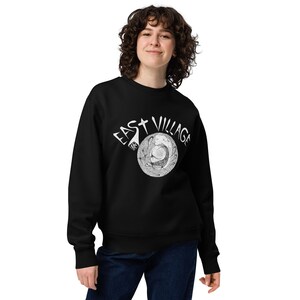 May include: Black sweatshirt with a white graphic print of a stylised circle with the text "East Village NYC" around it.