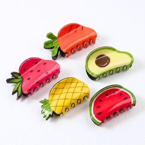 Könnte beinhalten: Ein Set aus fünf fruchtförmigen Haarspangen, bestehend aus einer roten Erdbeere mit grünen Blättern, einer orangefarbenen Karotte, einer gelben Ananas, einer grünen Avocado mit braunem Kern und einer roten Wassermelonenscheibe mit grüner Schale.