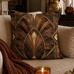 May include: A square throw pillow featuring a dark brown marble-textured background with a symmetrical, geometric fan pattern in gold lines. The design consists of radiating arcs and pointed shapes that create a structured, repeating motif.