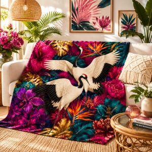 May include: A plush throw blanket featuring two white cranes with black wingtips and red crowns, set against a vibrant background of large pink, purple, and teal tropical flowers, orange bird of paradise blooms, and golden monstera leaves.