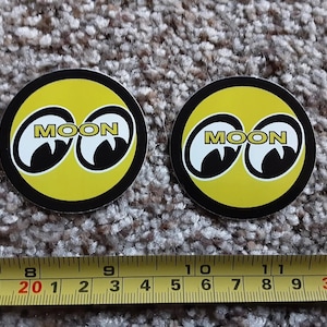 May include: Two yellow and black round stickers with the word "MOON" and two large black eyes.