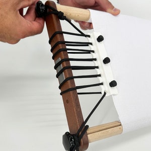 May include: A wooden embroidery hoop with black cord and white fabric stretched across it. The hoop has a white plastic piece with black buttons on it.