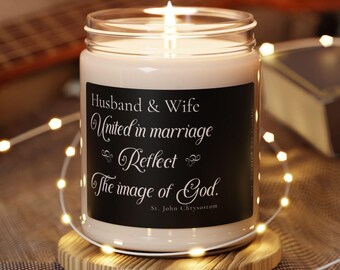 May include: A white candle with a black label that reads "Husband & Wife United in marriage Reflect The image of God. St. John Chrysostom". The candle is lit and sitting on a wooden coaster.