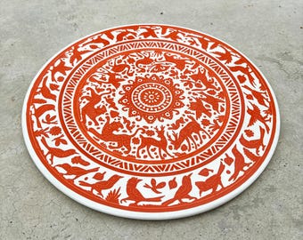 May include: A round, white ceramic plate with a vibrant orange design. The plate features a detailed pattern of animals, birds, and floral elements, creating a decorative and artistic piece. The plate is suitable for serving or display.