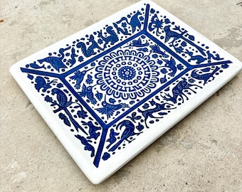 May include: A rectangular white ceramic tray with a detailed blue design. The design features a central circular pattern and various animal and bird silhouettes around the edges. The tray is likely used for serving or display.
