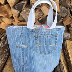 Könnte beinhalten: Eine blaue Jeans-Tragetasche mit weißen Henkeln. Die Tasche hat eine Tasche auf der Vorderseite und ein Blumenmuster-Futter.