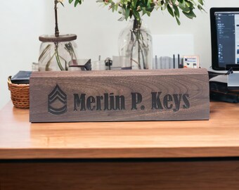 May include: A dark brown wooden desk nameplate with the text "Merlin P. Keys" and a black military rank insignia.