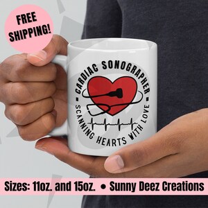 May include: White ceramic mug with a black and red design. The design features a heart with a stethoscope and a heartbeat line. The text reads "Cardiac Sonographer - Scanning Hearts With Love".