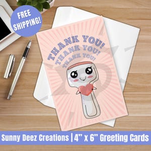 May include: A pink greeting card with the words "THANK YOU!" in blue. The card features a cartoon illustration of a spoon holding a heart. The card is 4" x 6" and comes with a white envelope.