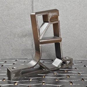 May include: A black 3D printed plastic bracket with a complex design. The bracket has a rectangular base and a vertical section with multiple openings.