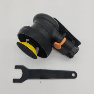 May include: A black and orange orbital sander with a yellow sanding pad and a black wrench. The sander has a curved handle and a round sanding base. The wrench is flat with a hole at the end.