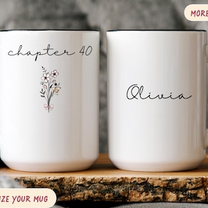 May include: White ceramic mug with a black handle and rim. The mug features the text "chapter 40" and a floral illustration on one side, and the name "Olivia" on the other. The mug is a personalized gift.