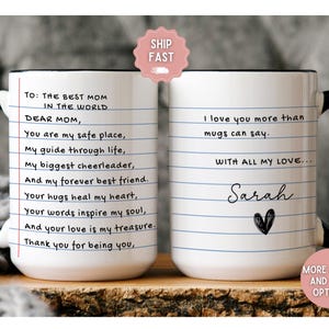 May include: White ceramic coffee mug with a black handle and black rim. The mug has a lined design and text that reads "To: The Best Mom in the World Dear Mom, You are my safe place, My guide through life, My biggest cheerleader, And my forever best friend. Your hugs heal my heart, Your words inspire my soul, And your love is my treasure. Thank you for being you." The other side of the mug has text that reads "I love you more than mugs can say. With all my love... Sarah" with a heart drawn below the name.
