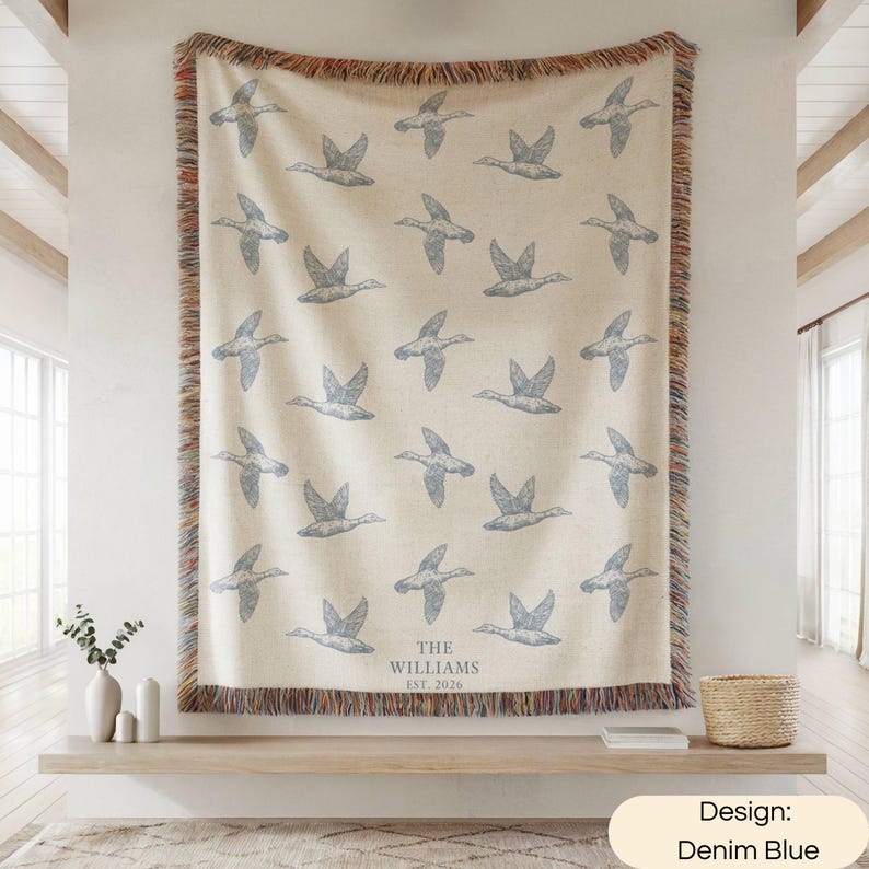 May include: A woven throw blanket with a cream background and a repeating pattern of flying ducks in denim blue. The bottom center features the text THE WILLIAMS EST. 2026. The blanket has a multicolored fringed edge on all four sides.