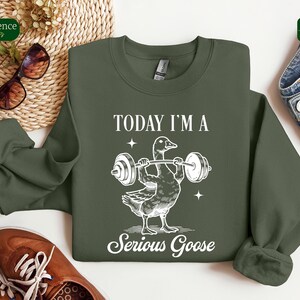 May include: A green sweatshirt with a white graphic of a goose lifting a barbell. The text "Today I'm a Serious Goose" is printed below the goose.