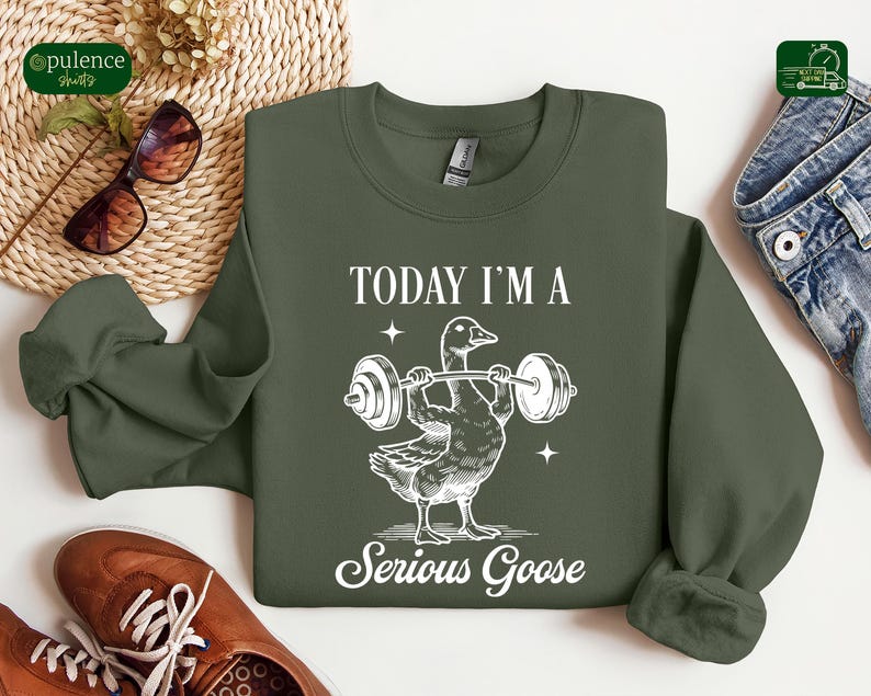May include: A green sweatshirt with a white graphic of a goose lifting a barbell. The text "Today I'm a Serious Goose" is printed below the goose.