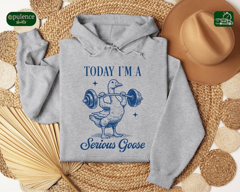May include: A gray hooded sweatshirt with the text "TODAY I'M A SERIOUS GOOSE" in blue. A cartoon goose is lifting a barbell with the text "TODAY I'M A" above the goose and "SERIOUS GOOSE" below the goose.