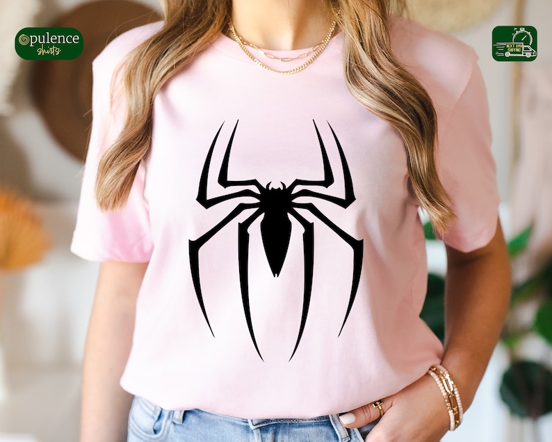 Puede incluir: Una camiseta rosa con un logotipo de Spiderman negro impreso en la parte delantera.