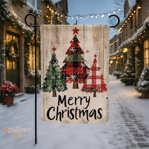 May include: A Christmas garden flag with three decorated Christmas trees in green, red, and black plaid patterns. The trees are set against a weathered wood background, with the words "Merry Christmas" in black script. A red star tops each tree.