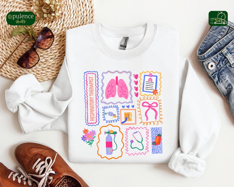 May include: White sweatshirt with colorful illustrations related to respiratory therapy. The design includes images of lungs, a stethoscope, and the text "RESPIRATORY THERAPIST" in a rectangular frame. The sweatshirt is paired with sunglasses and brown shoes.