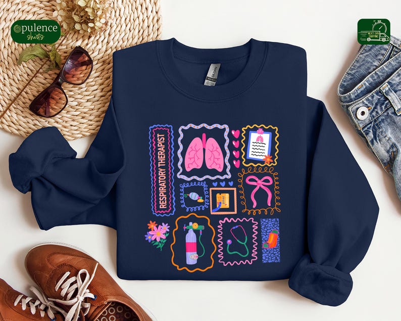 May include: Navy blue sweatshirt featuring a colorful graphic design. The design includes illustrations of lungs, a stethoscope, and other medical-related images, along with the text "Respiratory Therapist". The sweatshirt is a crew neck style.