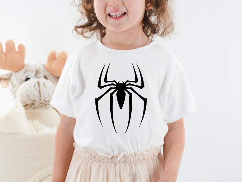 Puede incluir: Camiseta blanca con un gr&aacute;fico de ara&ntilde;a negra en la parte delantera.