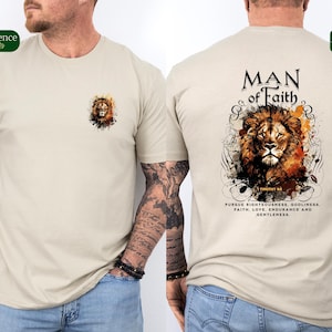 May include: Beige t-shirt featuring a lion graphic on the front and back. The front has a small lion graphic, while the back displays a larger lion design with the text "MAN of Faith" and inspirational text. The shirt is a crew neck.