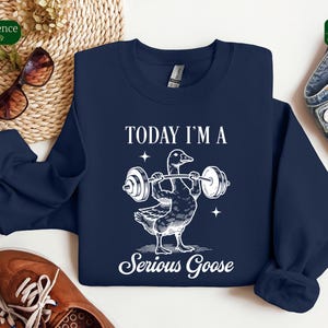 May include: A navy blue sweatshirt with a white graphic of a goose lifting weights. The text "Today I'm a Serious Goose" is printed below the goose.