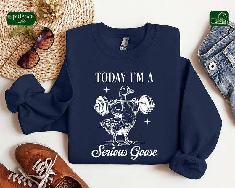 May include: A navy blue sweatshirt with a white graphic of a goose lifting weights. The text "Today I'm a Serious Goose" is printed below the goose.