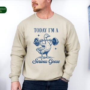 May include: A beige sweatshirt with a blue graphic of a goose lifting a barbell. The text "TODAY I'M A SERIOUS GOOSE" is printed on the sweatshirt.