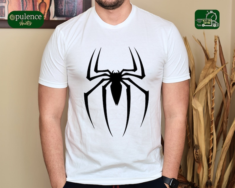 Puede incluir: Camiseta blanca con un logotipo de Spiderman negro impreso en la parte delantera.