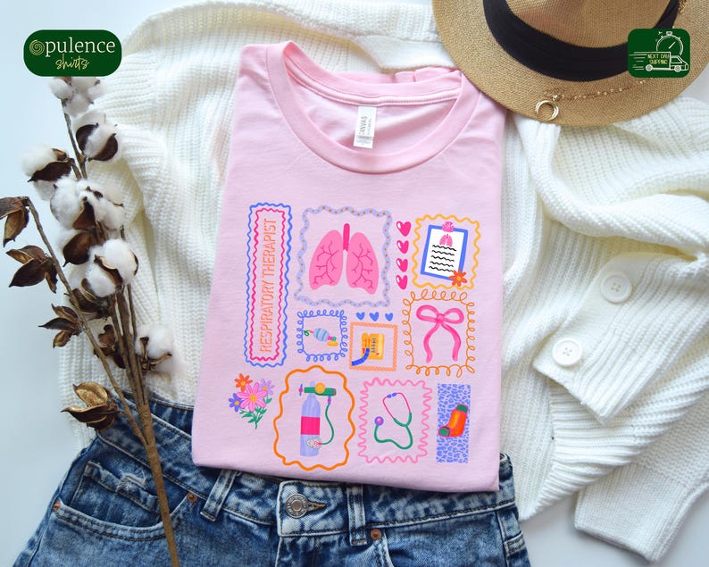 May include: A light pink t-shirt featuring a collage of medical-themed illustrations, including lungs, a stethoscope, and a bow. The words "RESPIRATORY THERAPIST" are printed vertically. The shirt is folded on top of blue jeans and a white sweater.