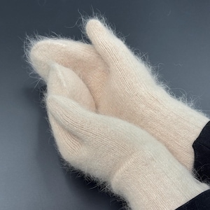May include: A pair of cream-colored mittens with a soft, fuzzy, and brushed texture. The mittens feature a simple knit construction with a ribbed cuff at the wrist, showcasing a light, airy appearance and a consistent, pale off-white color throughout.