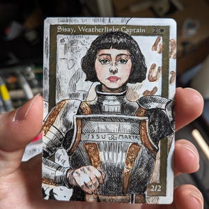 May include: A rectangular trading card featuring a hand-drawn illustration of a person with short dark hair wearing plate armor. The text Sisay, Weatherlight Captain is at the top, with JESU MARIA inscribed on the chest plate and 2/2 at the bottom.