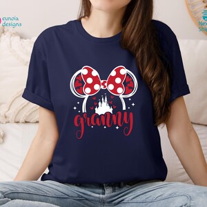 K&ouml;nnte beinhalten: Ein marineblaues T-Shirt mit einer wei&szlig;en Grafik eines roten und wei&szlig;en gepunkteten Bogens, eines wei&szlig;en Schlosses und dem Wort "granny" in Wei&szlig; mit roten Akzenten.