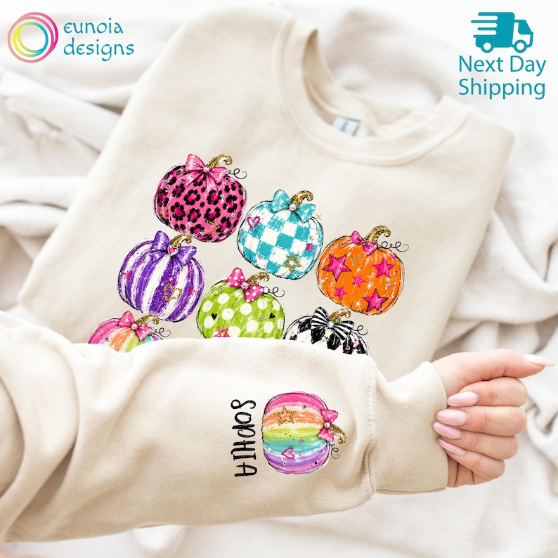 Puede incluir: Una sudadera de cuello redondo color beige con un estampado gr&aacute;fico de varias calabazas con diversos patrones, incluyendo estampado de leopardo, rayas, lunares y estrellas. La manga muestra una calabaza arco&iacute;ris con el nombre Sophia impreso verticalmente.