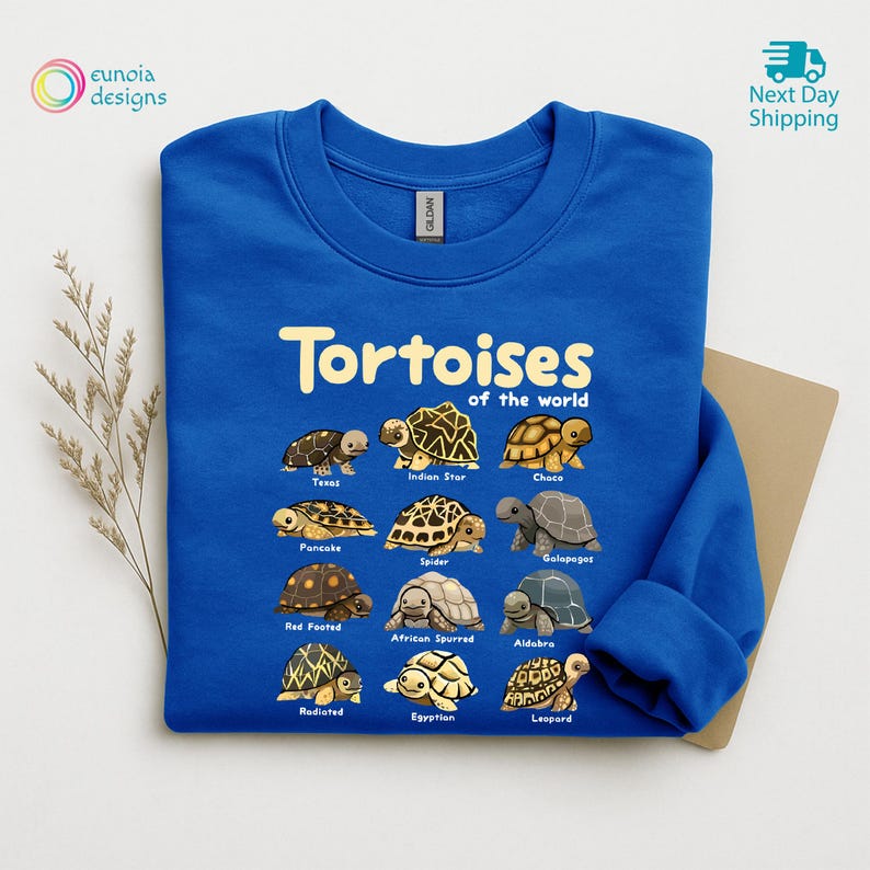 May include: A royal blue sweatshirt featuring the text "Tortoises of the World" above illustrations of various tortoise species. The sweatshirt has a crew neck and long sleeves. The brand name "Gildan" is visible.
