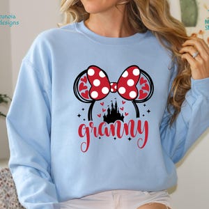 K&ouml;nnte beinhalten: Hellblauer Pullover mit einem roten und wei&szlig;en Minnie Mouse Ohren-Design und dem Wort "grammy" in roten und schwarzen Buchstaben.