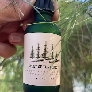 May include: A green glass spray bottle with a black cap and a white label. The label reads "SCENT OF THE FOREST" with a forest illustration and the text "FOREST BATHING MIST BODY & SPACE". The bottle contains 4 oz / 118 g.