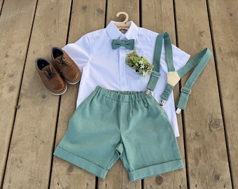 May include: A white button-down shirt with a green bow tie, a pair of brown leather shoes, and a pair of green suspenders with a small bouquet of flowers in the pocket. The shirt has the text "The Fashion Kids" on the hanger.