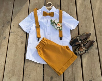 May include: A white button-down shirt with a bow tie, suspenders, and a flower boutonniere. The shirt is paired with mustard yellow shorts and brown snake-print loafers.