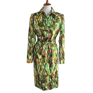 May include: A vintage long-sleeve dress with a vibrant floral pattern in shades of green, brown, yellow, and orange. The dress features a collared neckline, button-down front, and a matching belt. The dress is displayed on a mannequin.