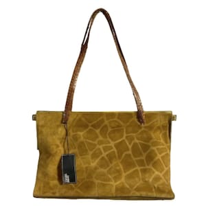 May include: A tan suede tote bag with a giraffe print pattern. The bag has brown leather handles and a rectangular shape. A black tag hangs from the bag.