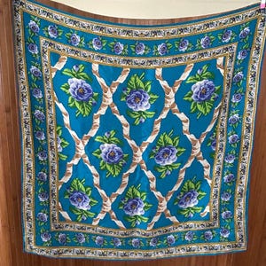 May include: A square scarf featuring a vibrant turquoise background with a repeating pattern of purple flowers and green leaves intertwined with beige ribbon-like lattice designs, framed by a decorative border of gold chains and small purple flowers.