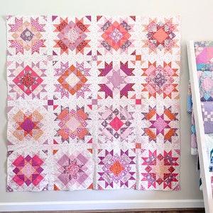 May include: A pink and white quilt with a patchwork design featuring various geometric shapes and floral patterns.