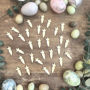 Peut inclure: Des découpes de carottes en bois et des œufs de Pâques mouchetés de différentes couleurs, dont rose, vert et bleu, sont disposés sur une surface en bois. De la verdure ajoute une touche naturelle à l'arrangement de Pâques.