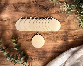 May include: A collection of eleven circular wooden ornaments, each featuring a small hole at the top for hanging. These light-colored, unfinished wood discs are arranged in a horizontal row with one additional disc placed separately below the main group.